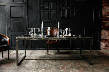 On a black wooden table are cutlery and white candlesticks. Against the background of black doors ....
