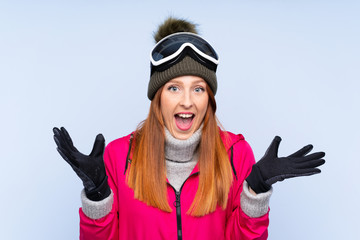 Skier redhead woman with snowboarding glasses over isolated blue wall unhappy and frustrated with something