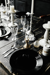 On a black wooden table are cutlery and white candlesticks. Against the background of black doors . Photozone . Gothic wedding table decoration