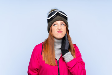 Skier redhead woman with snowboarding glasses over isolated blue wall thinking an idea