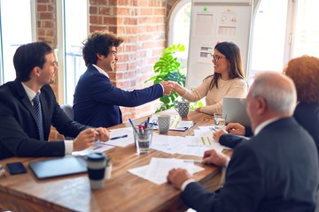 Group of business workers smiling happy and confident in a meeting. Speaking with smile on face working together shaking hands for agreement at the office.