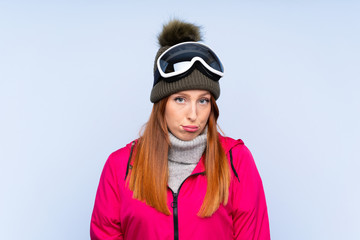 Skier redhead woman with snowboarding glasses over isolated blue wall sad