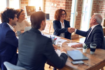 Group of business workers smiling happy and confident in a meeting. Speaking with smile on face working together shaking hands for agreement at the office.