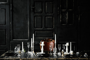 On a black wooden table are cutlery and white candlesticks. Against the background of black doors . Photozone . Gothic wedding table decoration - Powered by Adobe