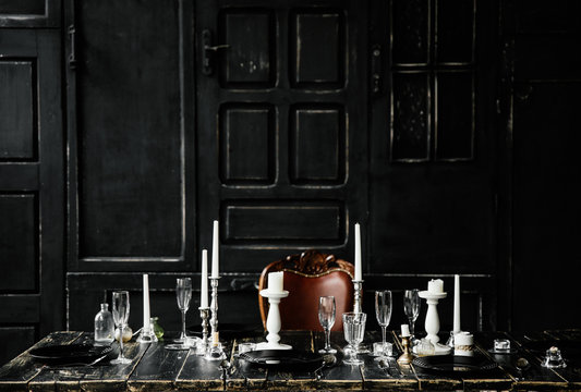 On a black wooden table are cutlery and white candlesticks. Against the background of black doors . Photozone . Gothic wedding table decoration