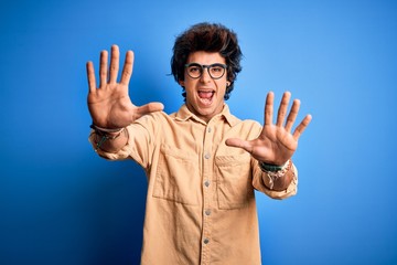 Naklejka premium Young handsome man wearing casual shirt standing over isolated blue background afraid and terrified with fear expression stop gesture with hands, shouting in shock. Panic concept.