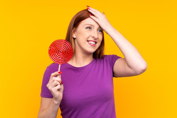 Young redhead woman holding a lollipop over yellow background has realized something and intending the solution