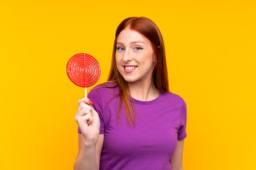 Young redhead woman holding a lollipop over yellow background