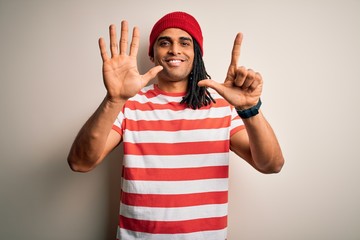 Young handsome african american man with dreadlocks wearing striped t-shirt and wool hat showing and pointing up with fingers number seven while smiling confident and happy.