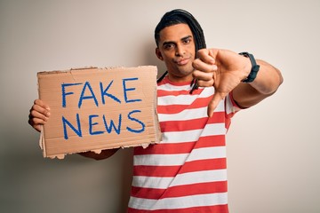 Young african american man with dreadlocks holding banner with fake news message protest with angry...