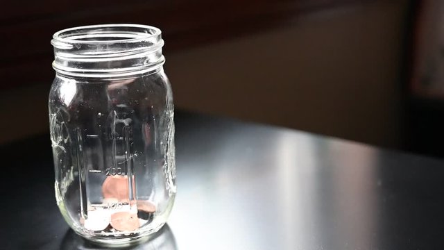 Slow motion of dropping coins into a glass jar