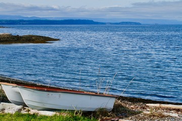 Fototapeta premium Two white rowboats on the shoreline in a blue bay on Hornby Island, BC. 