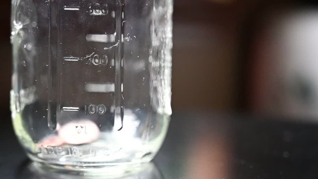 Slow motion of two fingers dropping coins into a glass jar