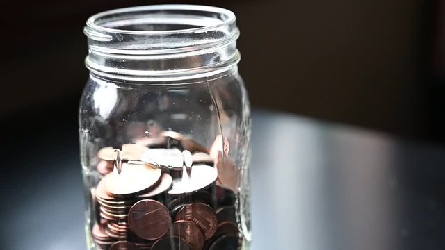 Slow motion of two fingers dropping coins into a glass jar