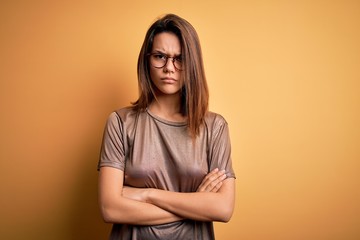 Fototapeta premium Beautiful brunette girl wearing casual t-shirt and glasses over isolated yellow background skeptic and nervous, disapproving expression on face with crossed arms. Negative person.