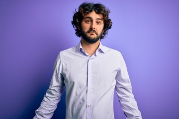 Young handsome business man with beard wearing shirt standing over purple background looking sleepy and tired, exhausted for fatigue and hangover, lazy eyes in the morning.