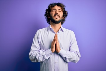 Young handsome business man with beard wearing shirt standing over purple background begging and praying with hands together with hope expression on face very emotional and worried. Begging.