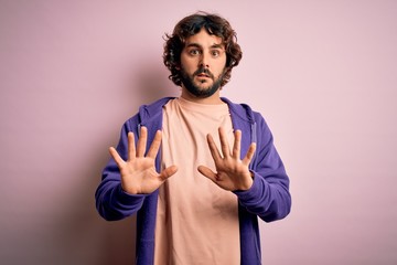 Young handsome sporty man with beard wearing casual sweatshirt over pink background Moving away...