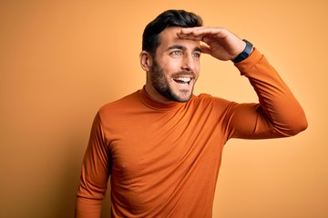 Young handsome man with beard wearing casual sweater standing over yellow background very happy and...