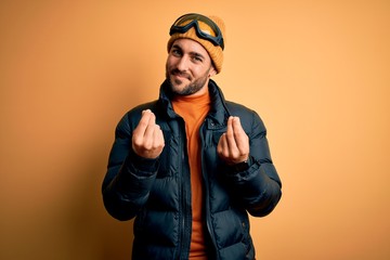 Young handsome skier man with beard wearing snow sportswear and ski goggles doing money gesture with hands, asking for salary payment, millionaire business