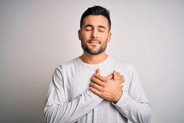 Young handsome man wearing casual t-shirt standing over isolated white background smiling with hands on chest with closed eyes and grateful gesture on face. Health concept.