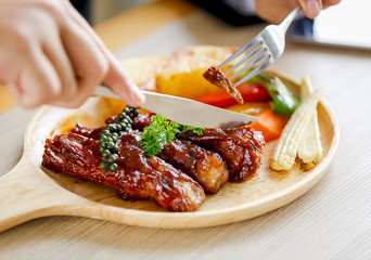 Grilled meat with vegetables on white plate, eating with fork and knife on table in restaurant