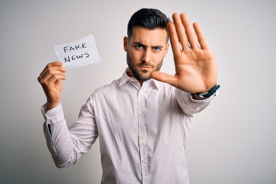 Young business man holding fake news paper over isolated background with open hand doing stop sign with serious and confident expression, defense gesture