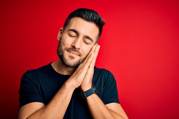 Young handsome man wearing casual black t-shirt standing over isolated red background sleeping tired dreaming and posing with hands together while smiling with closed eyes.