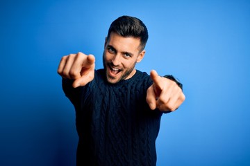 Fototapeta premium Young handsome man wearing casual sweater standing over isolated blue background pointing to you and the camera with fingers, smiling positive and cheerful