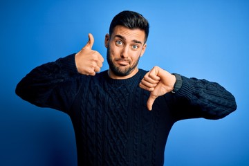 Young handsome man wearing casual sweater standing over isolated blue background Doing thumbs up...