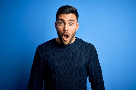 Young handsome man wearing casual sweater standing over isolated blue background afraid and shocked with surprise and amazed expression, fear and excited face.