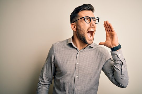 Young handsome man wearing elegant shirt and glasses over isolated white background shouting and screaming loud to side with hand on mouth. Communication concept.