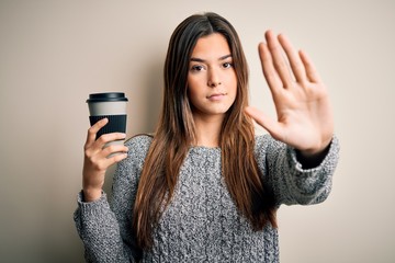 Young beautiful girl drinking cup of coffee standing over isolated white background with open hand doing stop sign with serious and confident expression, defense gesture