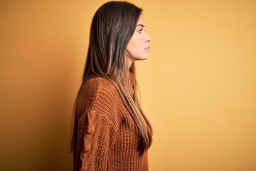 Young beautiful girl wearing casual sweater standing over isolated yellow background looking to...