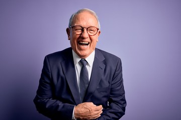 Grey haired senior business man wearing glasses and elegant suit and tie over purple background...