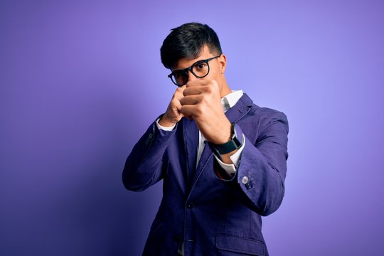 Young handsome business man wearing jacket and glasses over isolated purple background Punching fist to fight, aggressive and angry attack, threat and violence