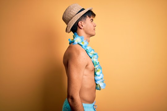 Young handsome tourist man on vacation wearing swimwear and hawaiian lei flowers looking to side, relax profile pose with natural face with confident smile.