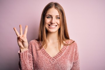 Young beautiful redhead woman wearing casual sweater over isolated pink background showing and pointing up with fingers number three while smiling confident and happy. - obrazy, fototapety, plakaty