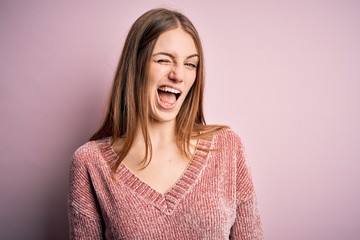 Fototapeta premium Young beautiful redhead woman wearing casual sweater over isolated pink background winking looking at the camera with sexy expression, cheerful and happy face.