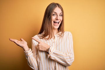 Fototapeta premium Young beautiful redhead woman wearing casual striped shirt over isolated yellow background amazed and smiling to the camera while presenting with hand and pointing with finger.