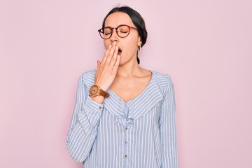 Young beautiful woman wearing casual striped shirt and glasses over pink background bored yawning tired covering mouth with hand. Restless and sleepiness.