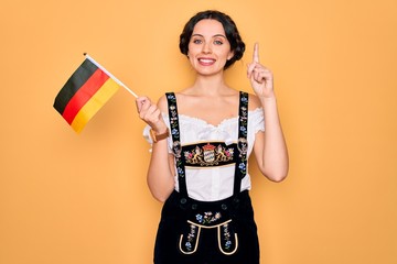 Young patriotic german woman with blue eyes wearing octoberfest dress holding germany flag surprised with an idea or question pointing finger with happy face, number one