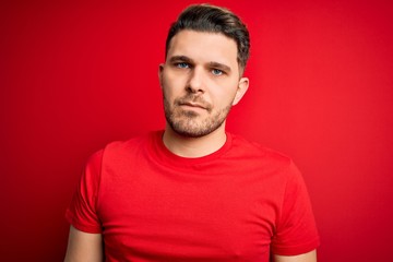 Obraz premium Young man with blue eyes wearing casual t-shirt over red isolated background with serious expression on face. Simple and natural looking at the camera.