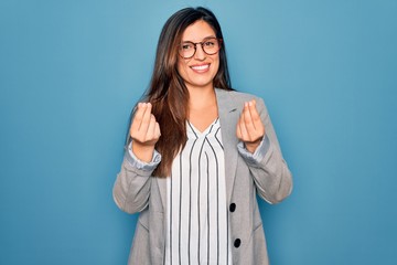 Young hispanic business woman wearing glasses standing over blue isolated background doing money gesture with hands, asking for salary payment, millionaire business