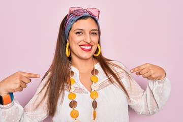 Young hispanic hippie woman wearing fashion boho style and sunglasses over pink background looking...