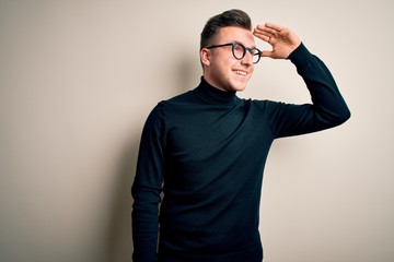 Young handsome caucasian man wearing glasses and casual sweater over isolated background very happy and smiling looking far away with hand over head. Searching concept.