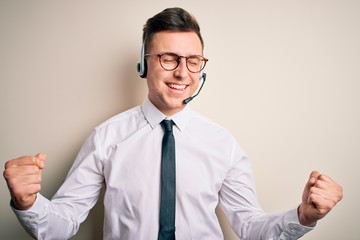 Young handsome caucasian business man wearing call center headset at customer service very happy and excited doing winner gesture with arms raised, smiling and screaming for success. Celebration 