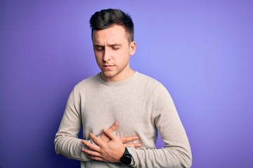 Young handsome caucasian man wearing casual sweater over purple isolated background with hand on stomach because indigestion, painful illness feeling unwell. Ache concept.