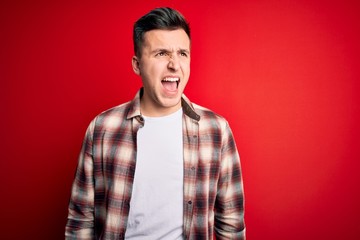 Young handsome caucasian man wearing casual modern shirt over red isolated background angry and mad screaming frustrated and furious, shouting with anger. Rage and aggressive concept.