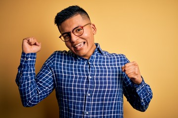 Naklejka premium Young handsome latin man wearing casual shirt and glasses over yellow background Dancing happy and cheerful, smiling moving casual and confident listening to music